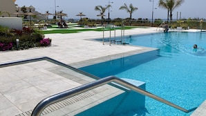 Une piscine avec une terrasse carrelée, des palmiers et un ciel dégagé.