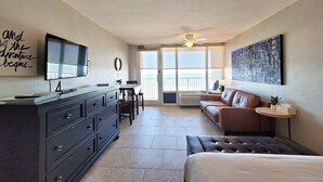 A hotel room with a bed, a TV mounted on the wall, a dresser, a sofa, a small table, and a large window with a view.