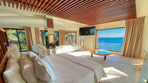 A modern hotel room with a large bed, a round coffee table, a TV, and a balcony with a view of the sea. - Esplendor by Wyndham Isla Mujeres Boutique All Inclusive (Isla Mujeres)