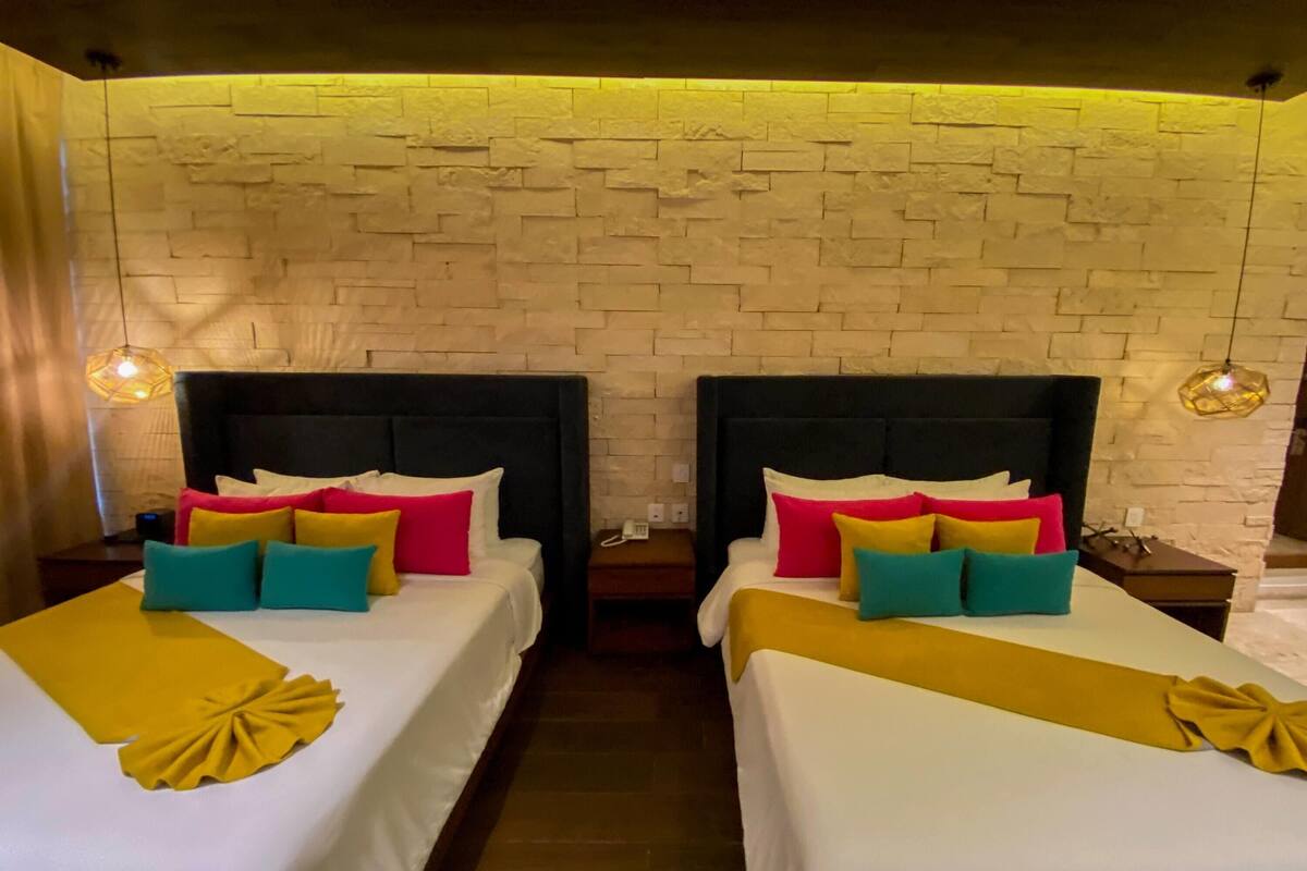 A hotel room with two beds, each with a headboard, pillows, and a blanket.