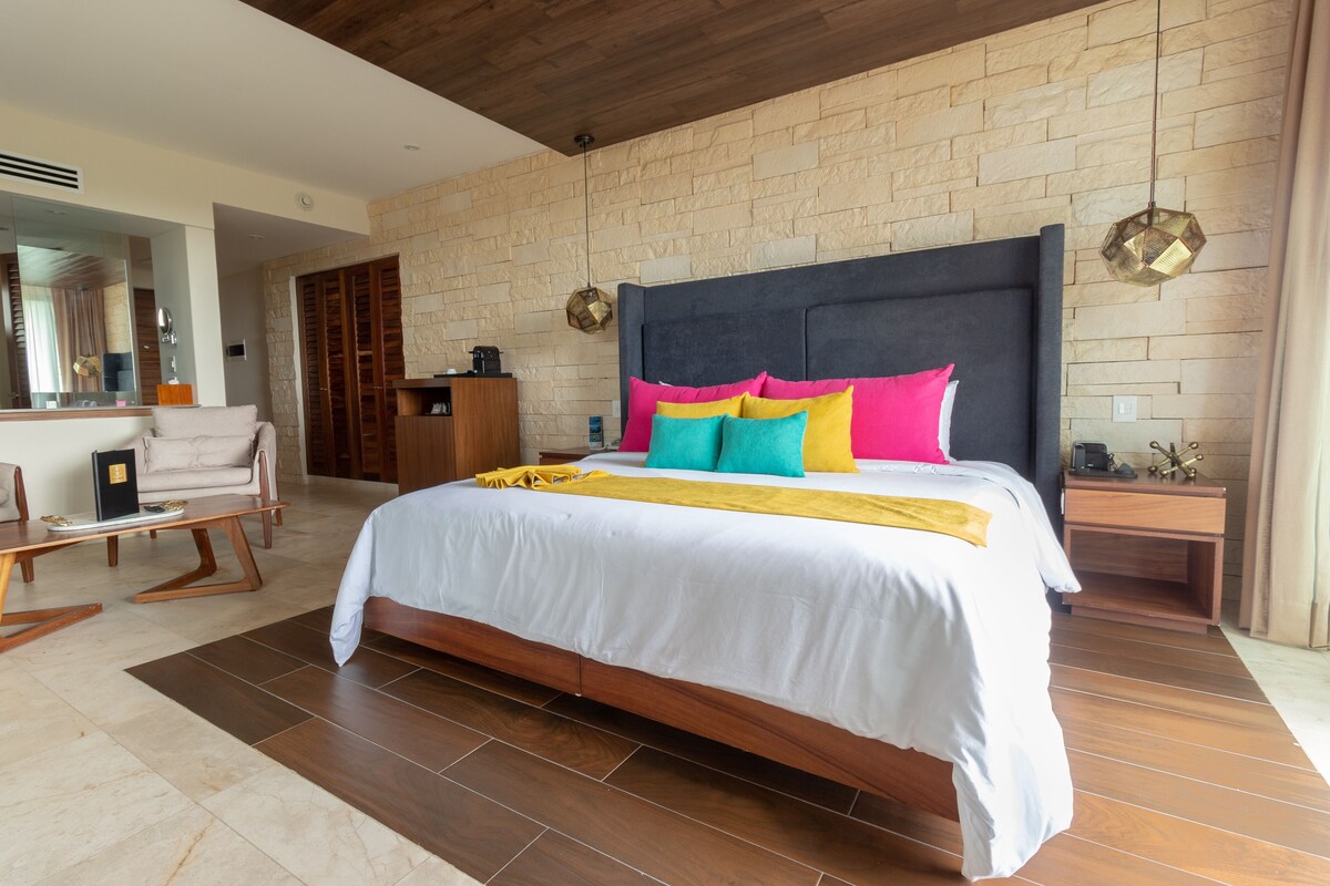 A modern bedroom with a large bed, a wooden headboard, and a stone wall.