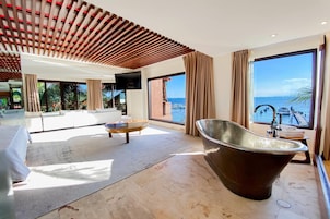 A modern hotel room with a large bathtub, a sofa, a coffee table, and a TV.