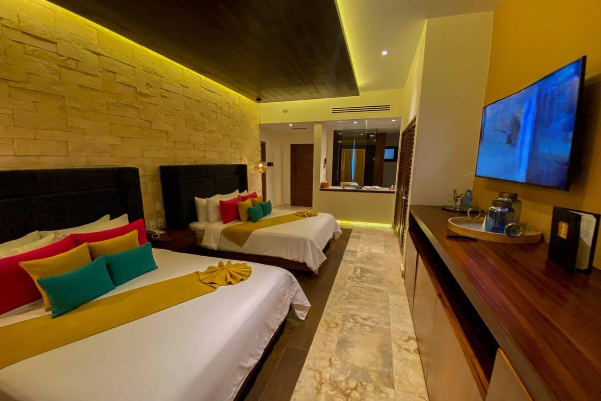 A hotel room with two beds, a wooden headboard, a TV on the wall, and a marble floor.