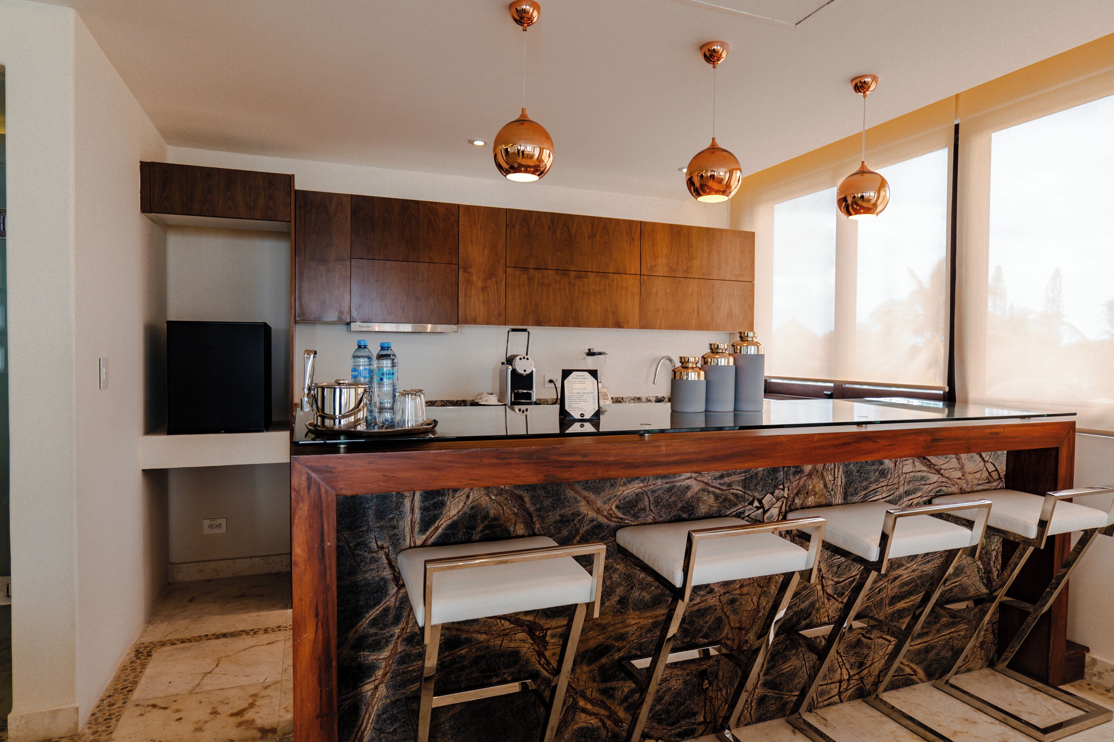 A modern kitchen with a marble island, bar stools, pendant lighting, and a large window.
