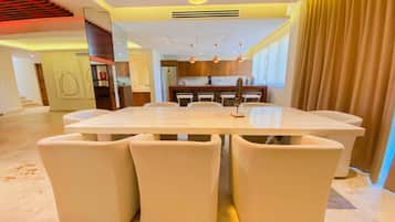 Un comedor moderno con una mesa de mármol y sillas blancas, una cocina al fondo y una escalera que sube a un nivel superior.