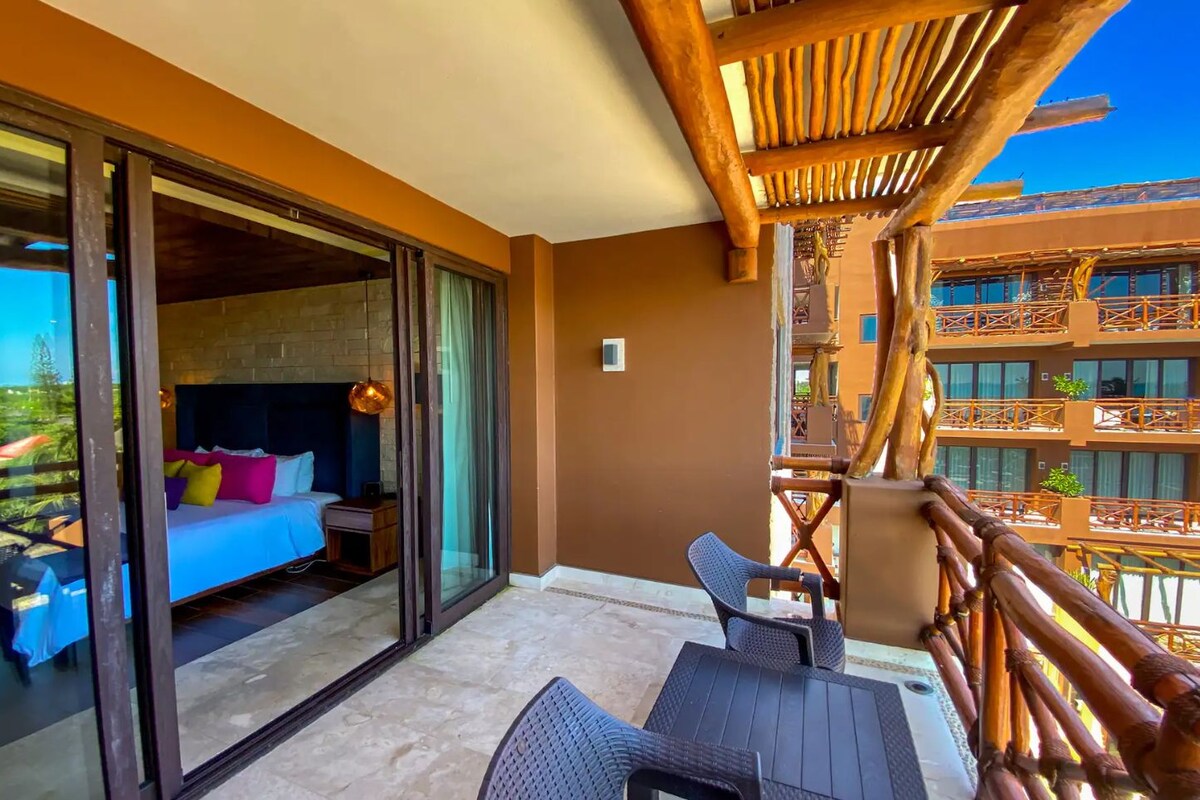 A balcony with a bed, a table, and chairs, and a view of a building with balconies.