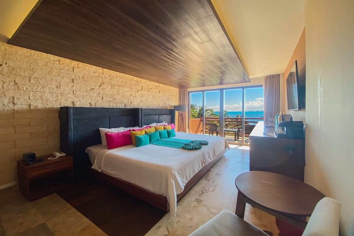 A bedroom with a large bed, a wooden ceiling, a stone wall, and a view of the ocean.