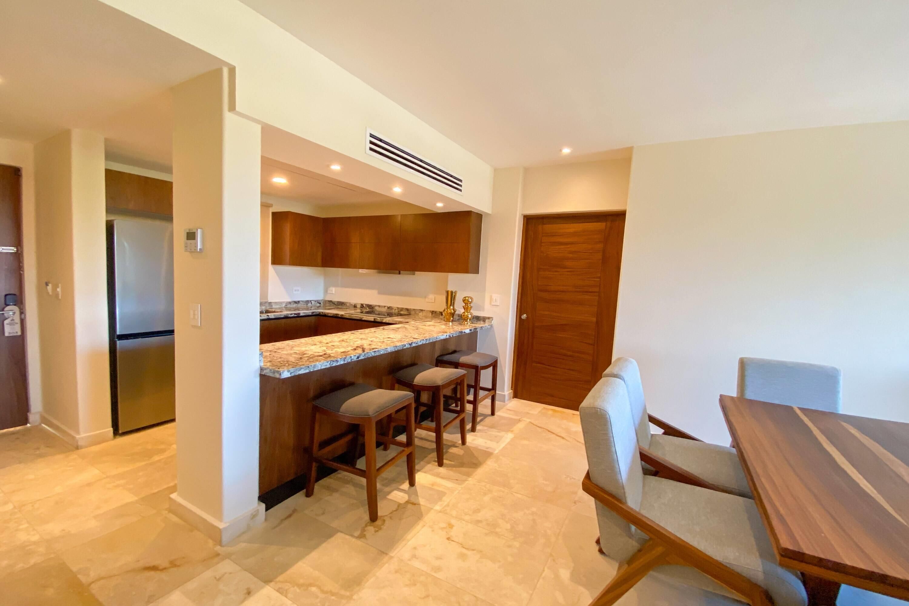 A modern kitchen with a built-in island, bar stools, and a dining table with chairs.