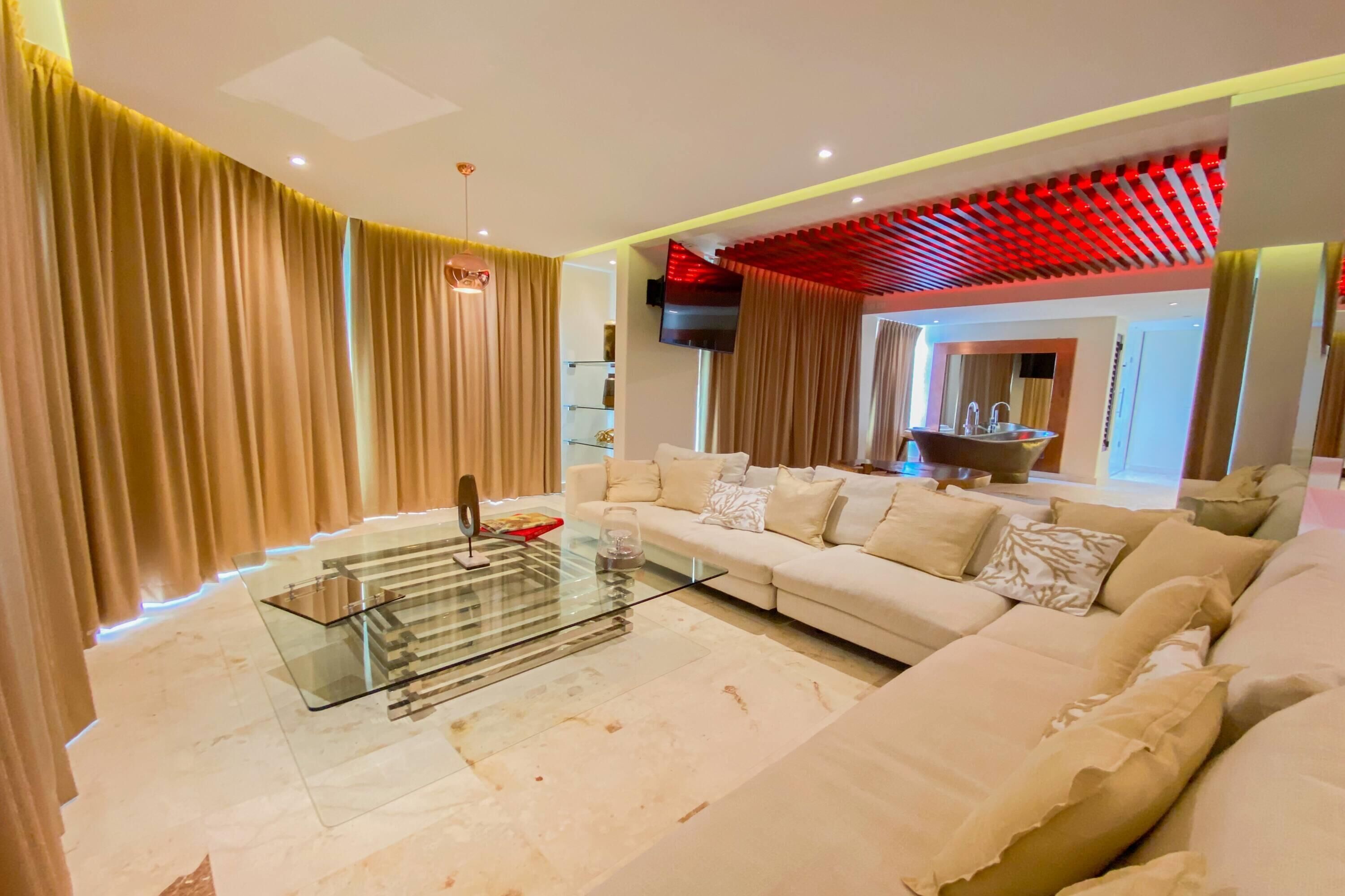 A modern living room with a glass coffee table, beige sofa, and curtains.