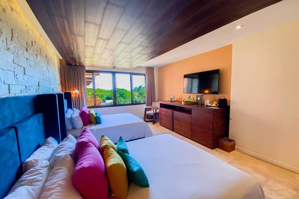A hotel room with two beds, a TV, a desk, and a window with a view.