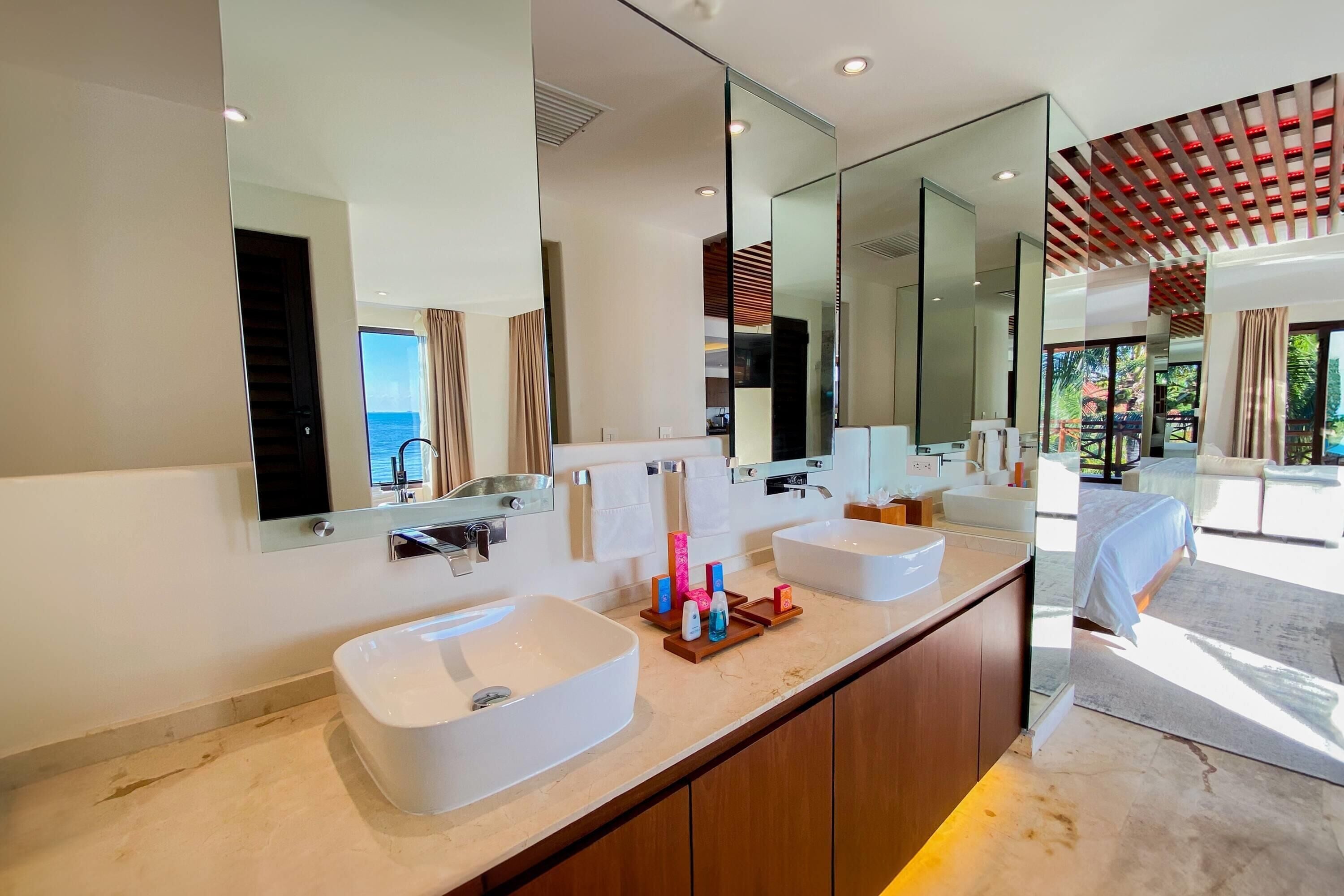 A modern bathroom with two sinks, a large mirror, and a view of the outdoors.