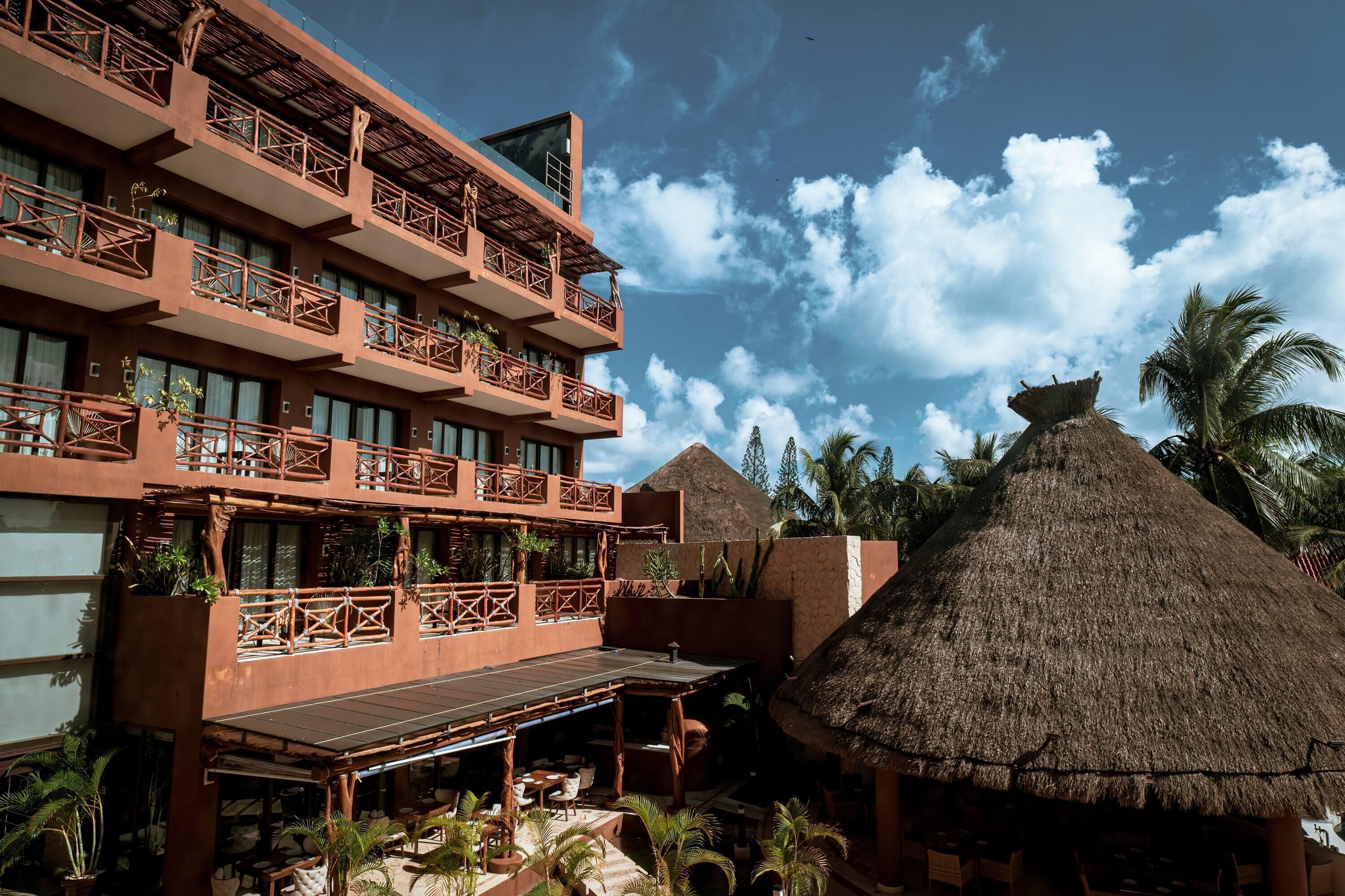 A multi-story hotel with balconies, a thatched-roof structure, and outdoor seating.