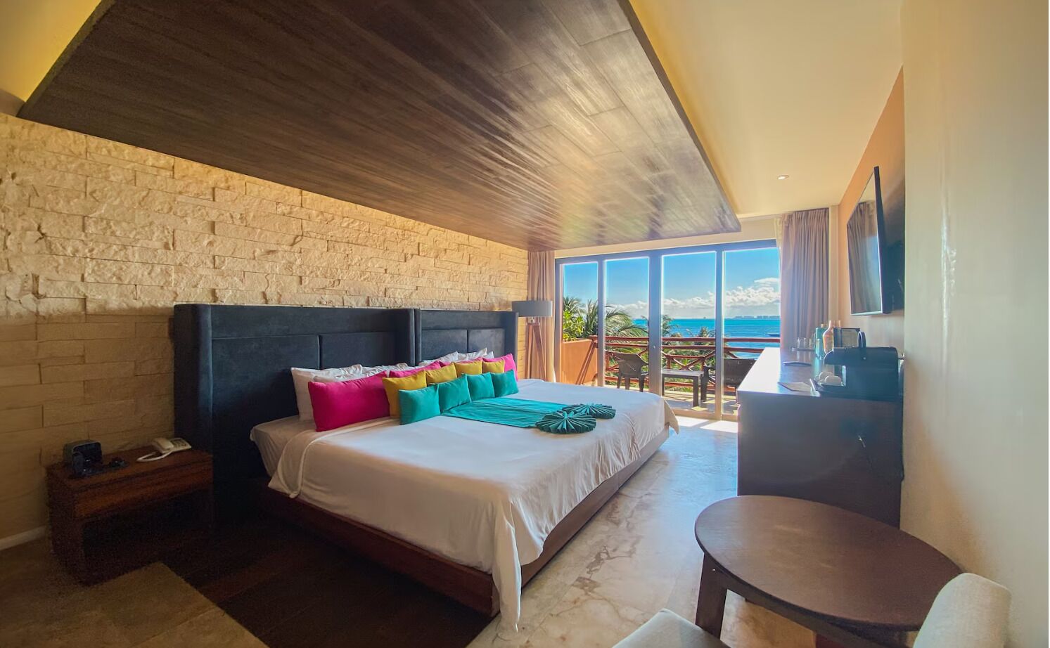 Un dormitorio con una cama grande, cabecera de madera, mesita de noche, escritorio y vista al océano.