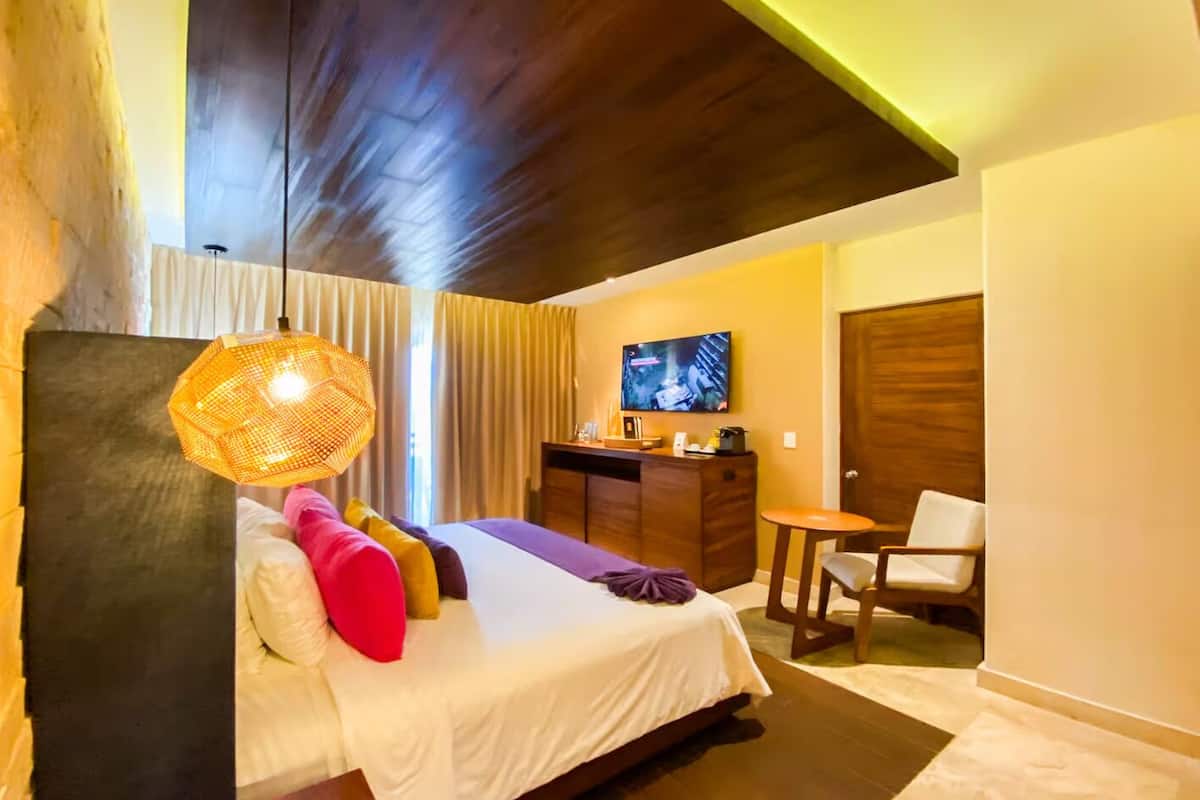 A modern hotel room with a bed, a desk, a chair, and a television.