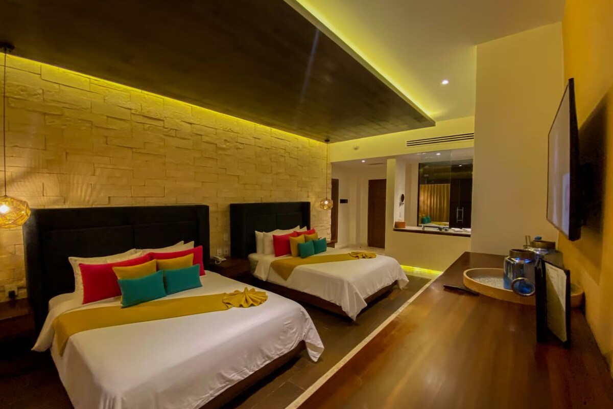 A hotel room with two beds, a brick wall, a wooden floor, a TV, and a small table with a lamp.