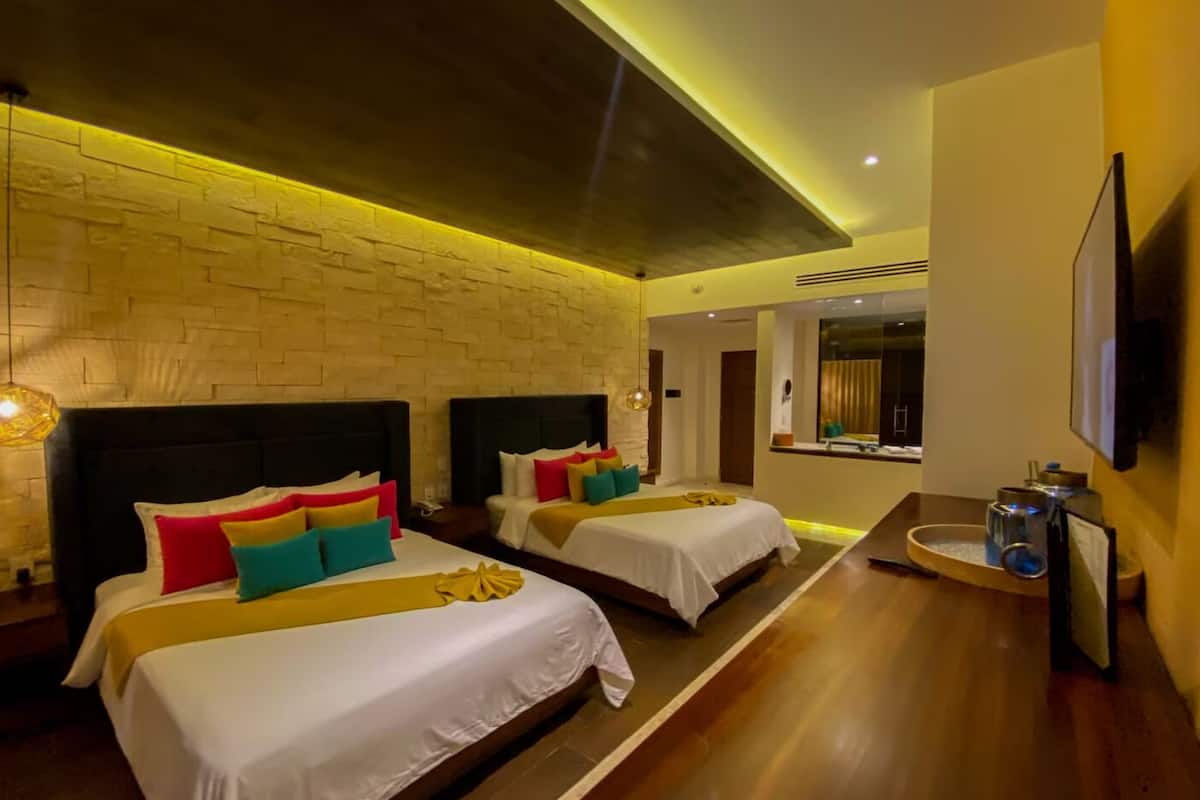 A hotel room with two beds, a brick wall, a wooden floor, a TV, and a small table with a lamp.