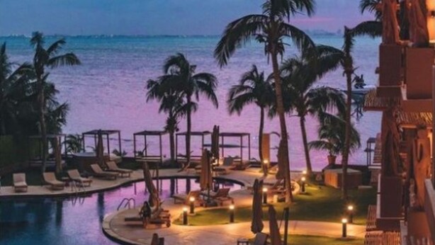 A resort pool area with lounge chairs and umbrellas, surrounded by palm trees and overlooking the ocean. - Esplendor by Wyndham Isla Mujeres Boutique All Inclusive (Isla Mujeres)