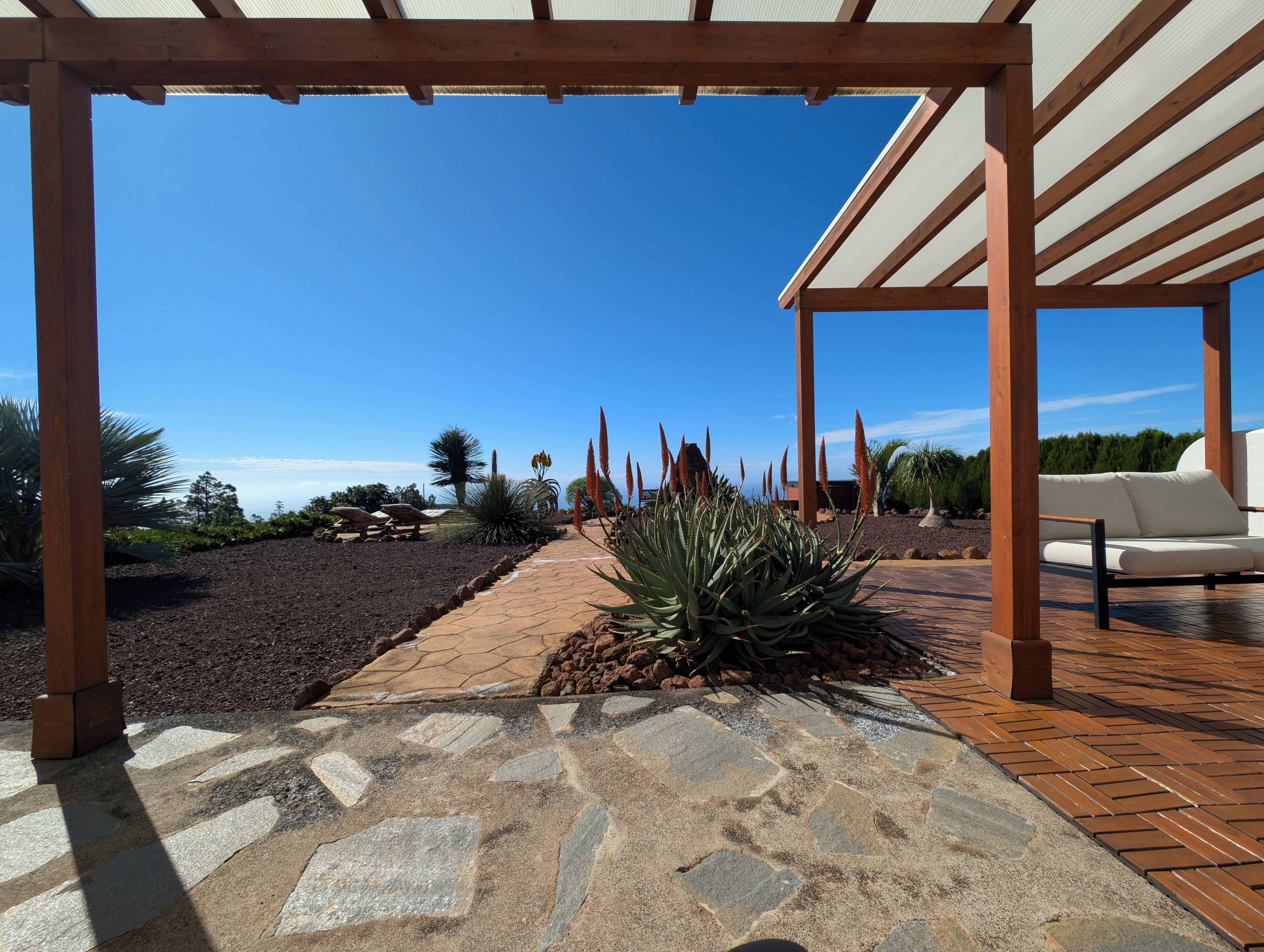 A covered outdoor area with a stone pathway, wooden pergola, and a seating area with a white sofa.