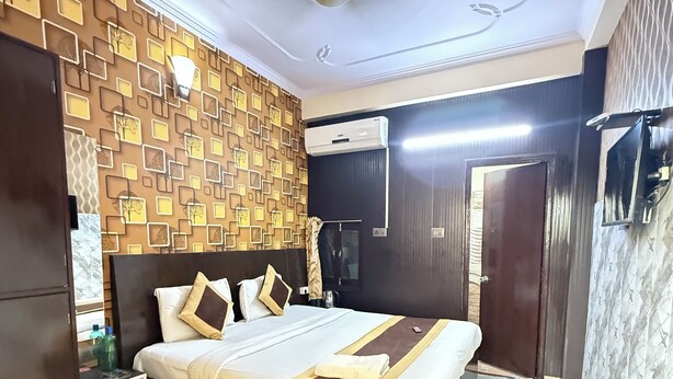 A hotel room with a large bed, a ceiling fan, an air conditioning unit, and a patterned wall. - Hotel Prakash Palace (Varanasi)