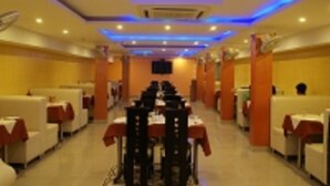 A restaurant with booths and tables, blue ceiling lights, and a TV screen. - Hotel Prakash Palace (Varanasi)