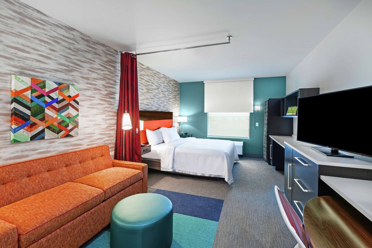 A modern hotel room with a sofa, bed, desk, and TV.