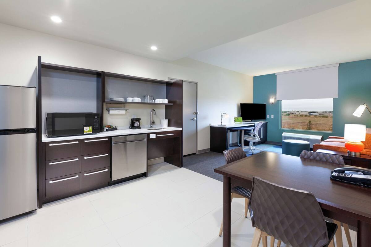 A modern kitchen with stainless steel appliances, a dining area with a table and chairs, and a view of the outdoors through a window.