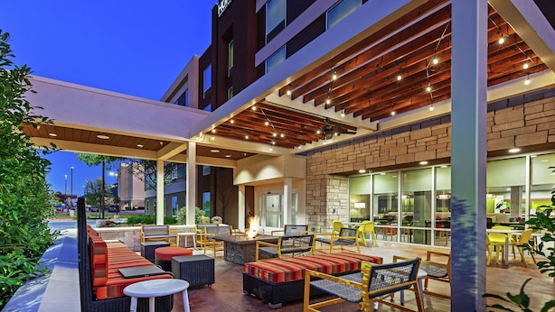 An outdoor seating area with sofas, chairs, and tables, connected to a building with a brick facade and a sign reading "HOME 2". - Home2 Suites by Hilton Abilene (Abilene)