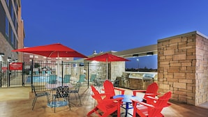 An outdoor patio with red Adirondack chairs, a pool, and a barbecue area. - Home2 Suites by Hilton Abilene (Abilene)
