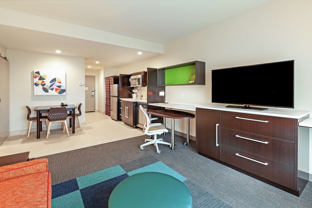 A modern living room with a dining area, kitchenette, and a flat-screen TV.