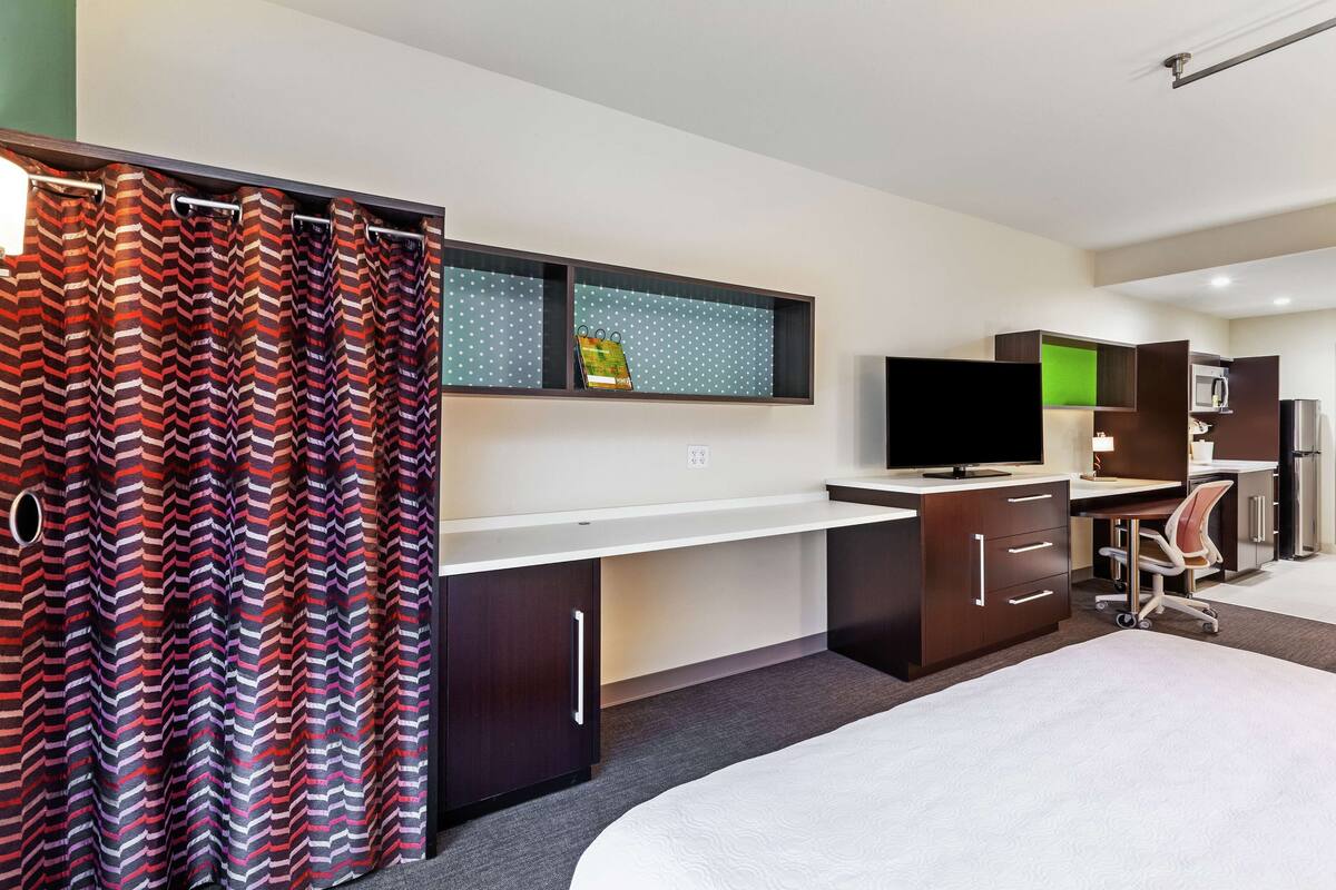 A hotel room with a bed, a desk, a chair, a TV, and a wardrobe.