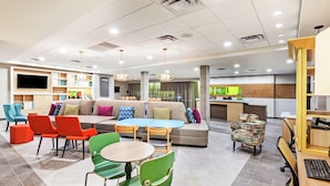 A modern hotel lobby with a sofa, chairs, a dining area, and a kitchen in the background. - Home2 Suites by Hilton Abilene (Abilene)
