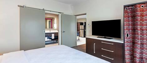 Une chambre d’hôtel avec un lit, une télévision, une armoire et une salle de bain, visibles à travers une porte ouverte.