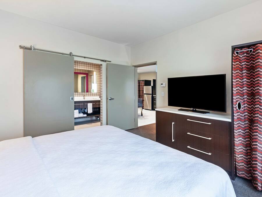 A hotel room with a bed, a TV, a wardrobe, and a bathroom visible through an open door.