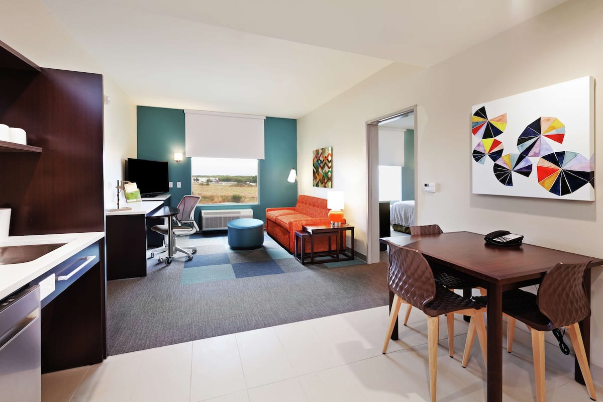 A modern living room with a dining area, a kitchen, and a large window with a view.