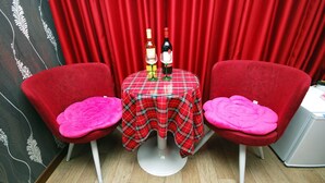 A room with two red velvet chairs, a plaid table, and a bottle of wine. - M Motel (Gangneung)