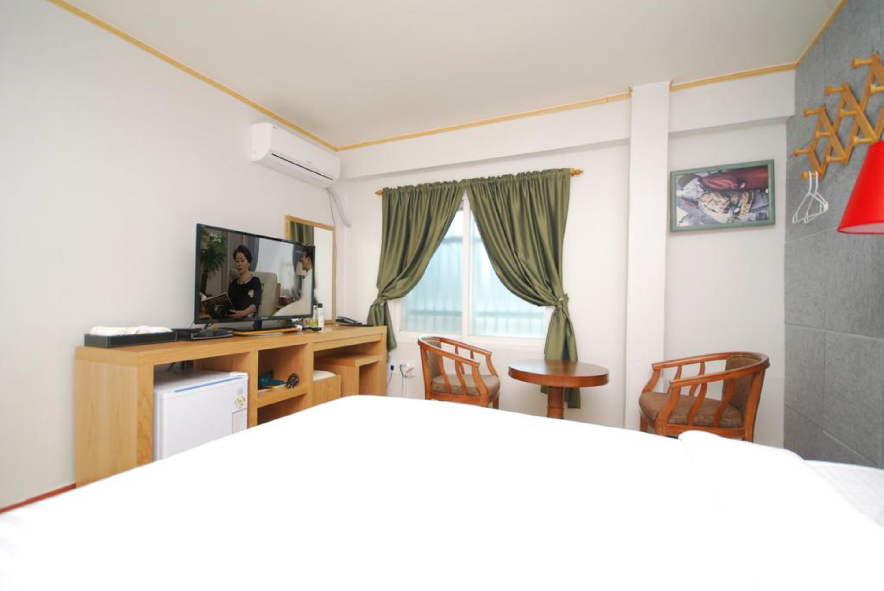A hotel room with a bed, a desk with a computer, two chairs, a small table, and a window with curtains.