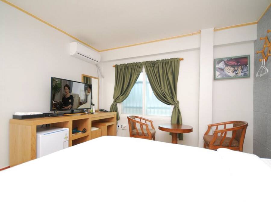 A hotel room with a bed, a desk with a computer, two chairs, a small table, and a window with curtains.