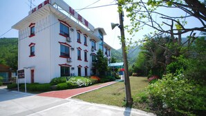 A multi-story building with a red and white facade, surrounded by greenery and a clear sky. - M Motel (Gangneung)