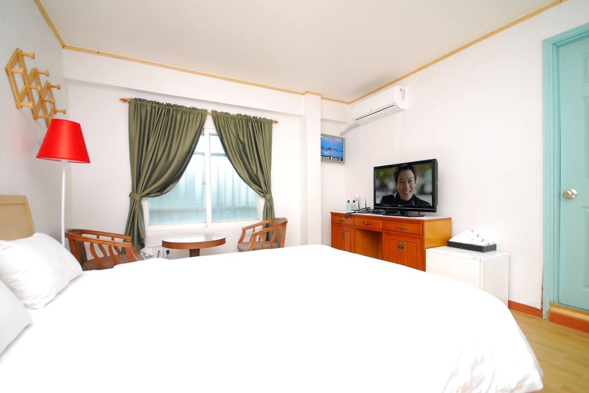 Quarto de hotel com cama, escrivaninha, cadeira, televisão e janela com cortinas.