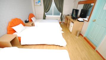 Habitación de hotel con una cama grande, un escritorio con computadora, un televisor y una ventana con cortinas.