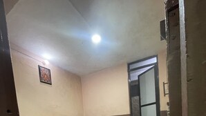 A room with a bed, a nightstand, a wooden herringbone floor, a ceiling light, and a door leading to another room. - Nirvaan Guest House (Kathmandu)