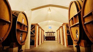 A wine cellar with wooden barrels arranged in rows, a central table, and a chandelier. - Charming cottage located in the heart of a Provencal farmhouse and its winery (Le Plan du Castellet)