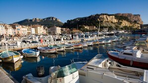 A marina with various boats docked, a rocky hill in the background, and buildings along the waterfront. - Charming cottage located in the heart of a Provencal farmhouse and its winery (Le Plan du Castellet)