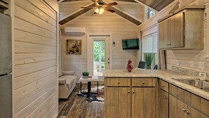 A wooden interior with a kitchen area, a dining table with chairs, and a ceiling fan. - Little Red Roof, a tiny house in the GA mountains! (Clayton)