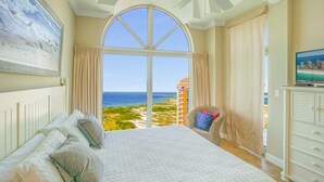 Un dormitorio con una cama grande, vista al océano, una silla y un televisor.