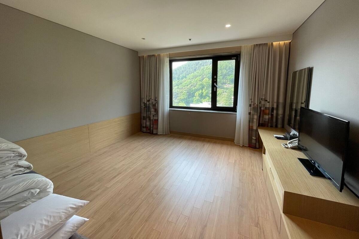 A modern hotel room with a large window, a flat-screen TV, and a wooden floor.