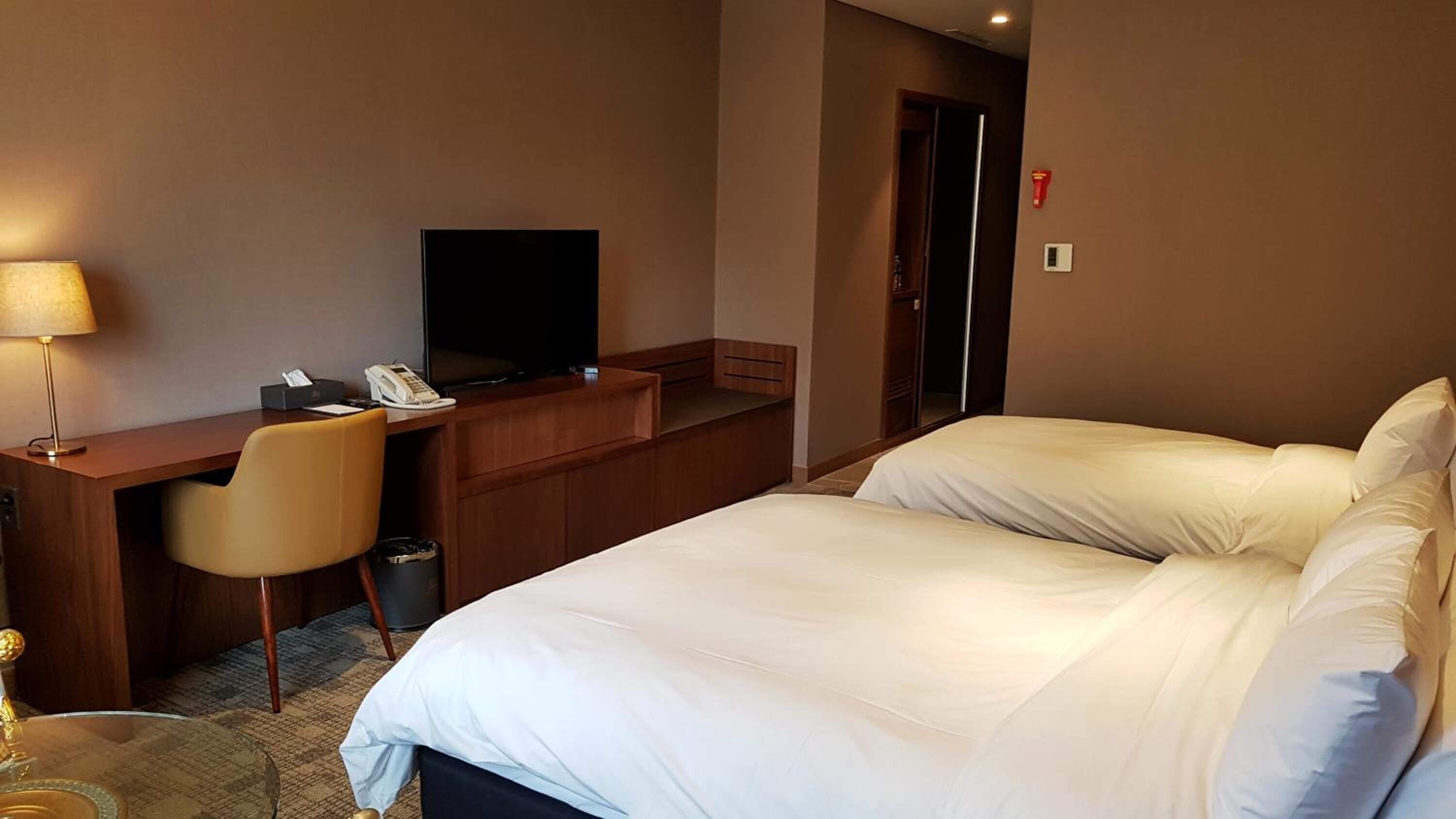 A hotel room with a bed, a desk with a chair, a television, and a telephone.