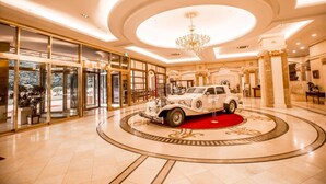 Un lobby imponente con un coche clásico en exhibición, elegantes candelabros y un piso circular de mármol.