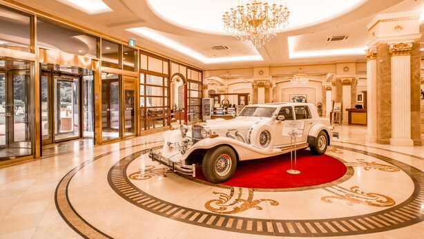 Un vestíbulo imponente con un coche clásico expuesto, elegantes candelabros y una alfombra roja.