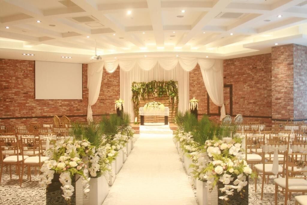 A wedding venue with a central aisle, floral arrangements, and a brick wall backdrop.